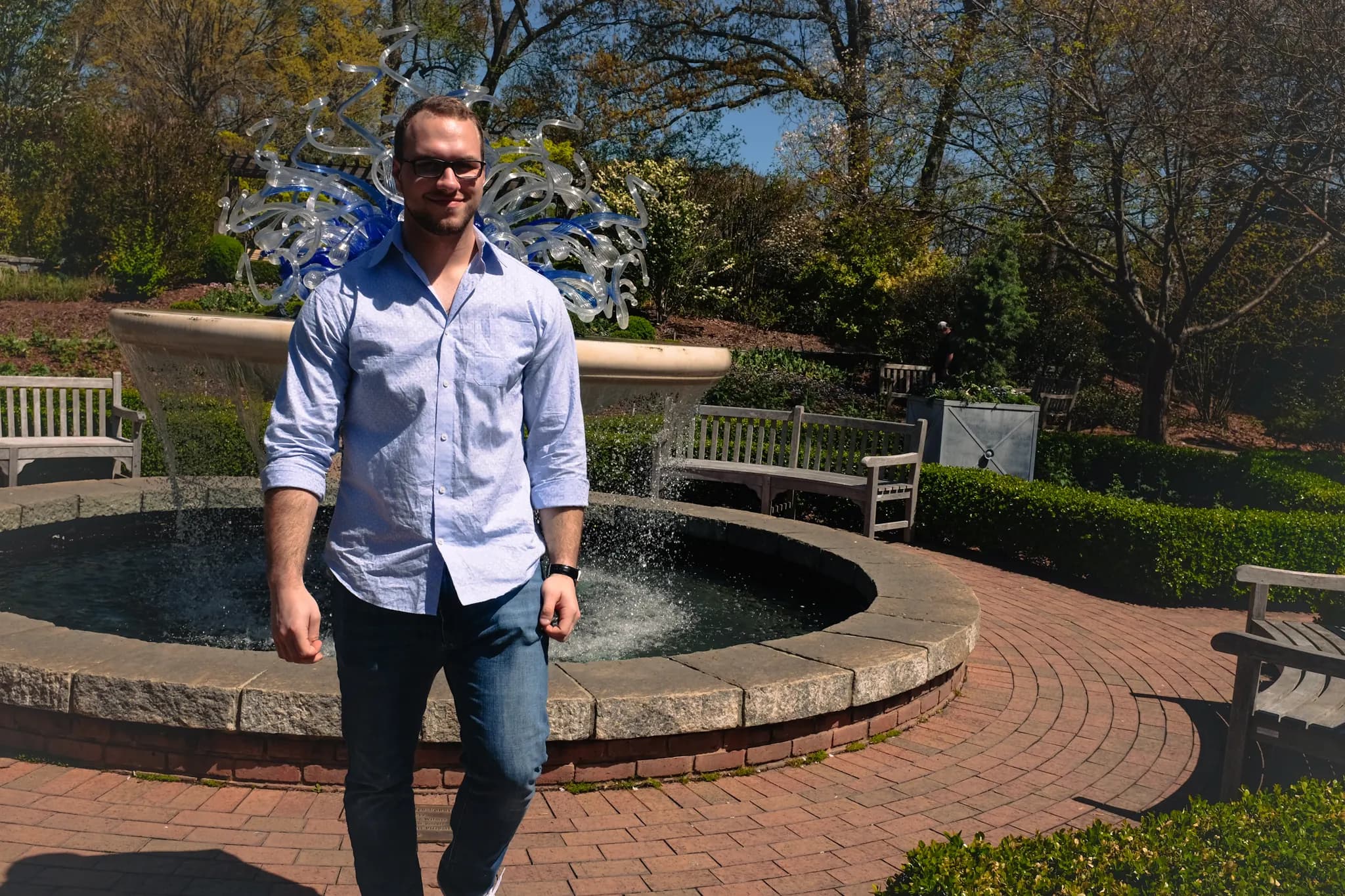 Tyler Henn standing beside a garden fountain with a blue glass sculpture