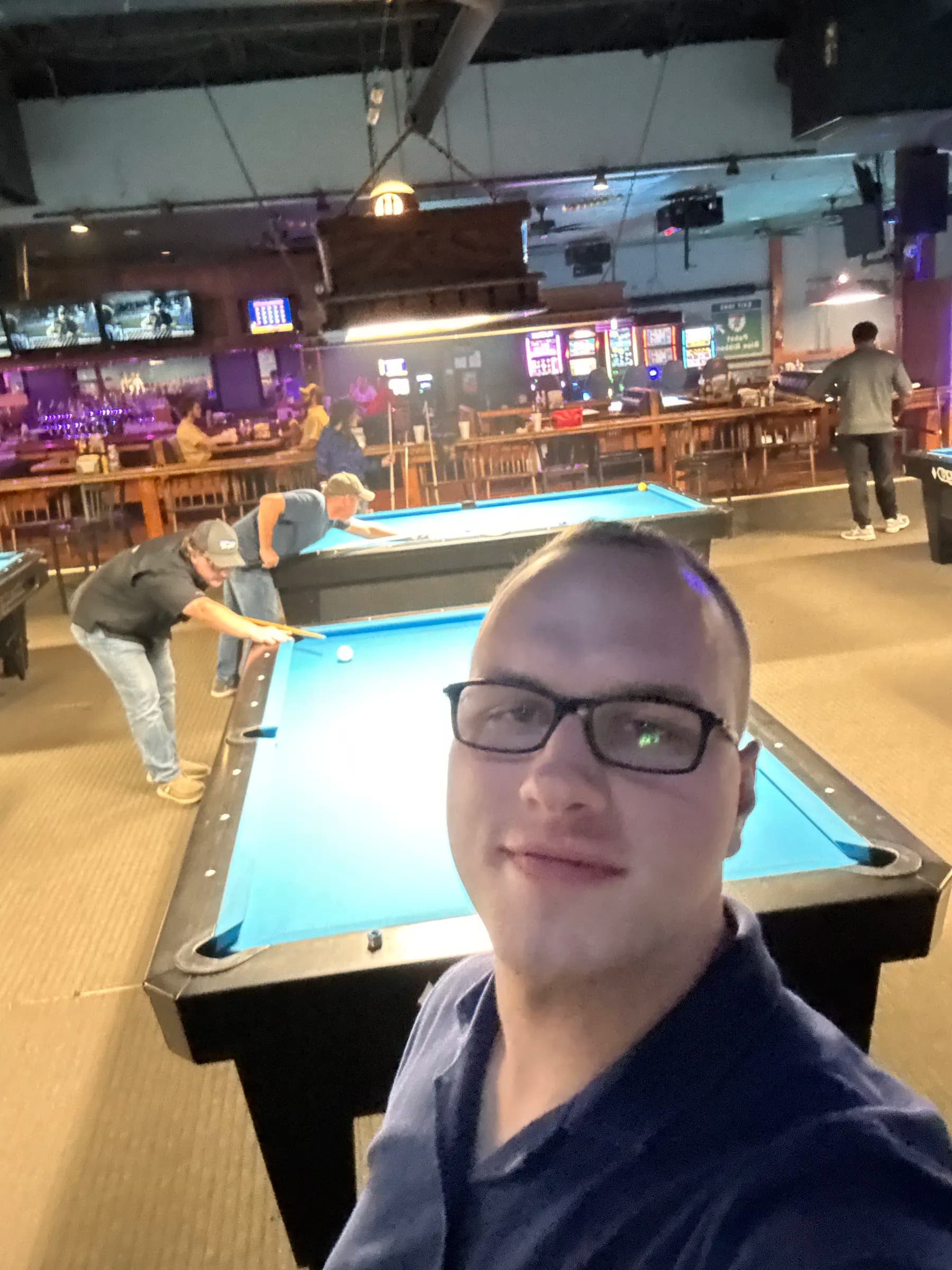 Tyler Henn taking a selfie inside a pool hall with billiards tables behind him