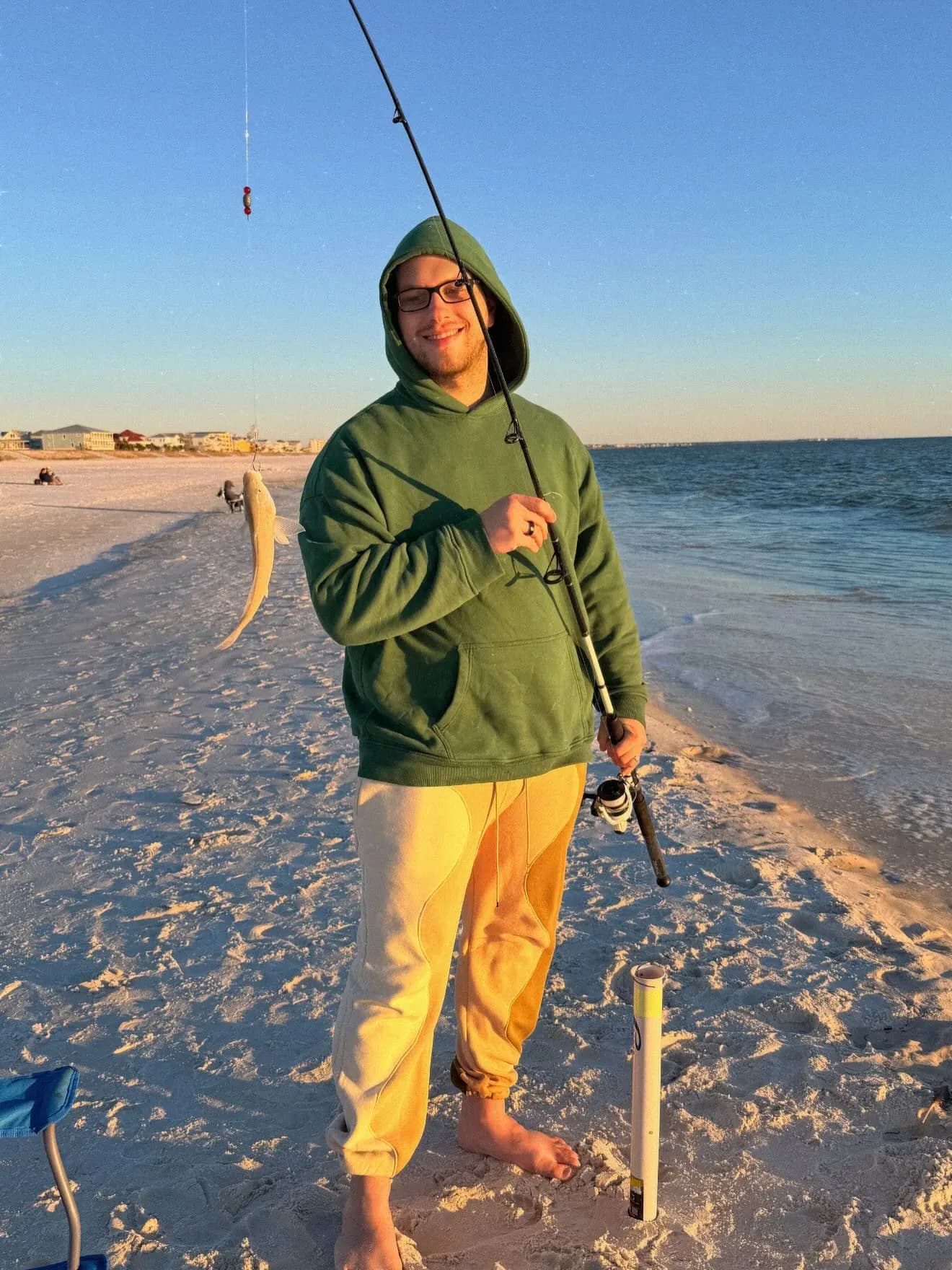 Tyler Henn holding a fishing rod after catching a fish from a sandy beach