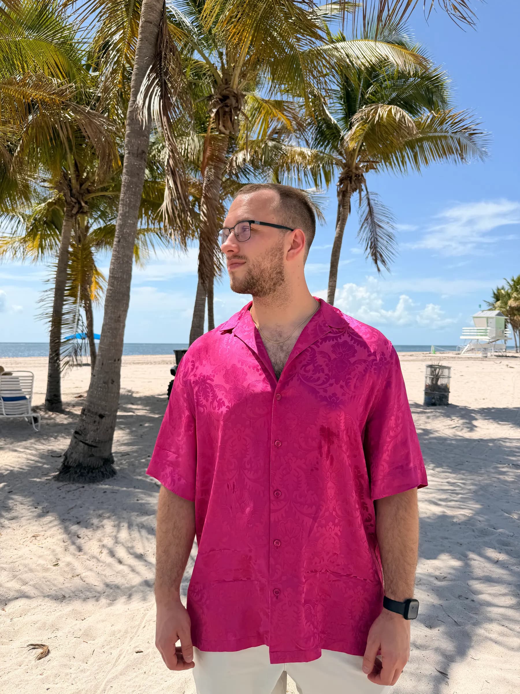 Tyler Henn wearing a bright pink shirt beneath palm trees on a beach in Miami, Florida