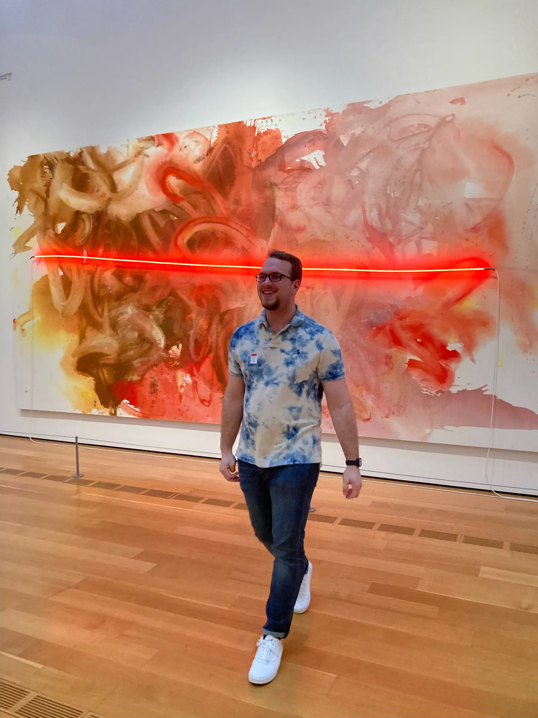 Tyler Henn standing in front of a large red and orange abstract painting at an art gallery