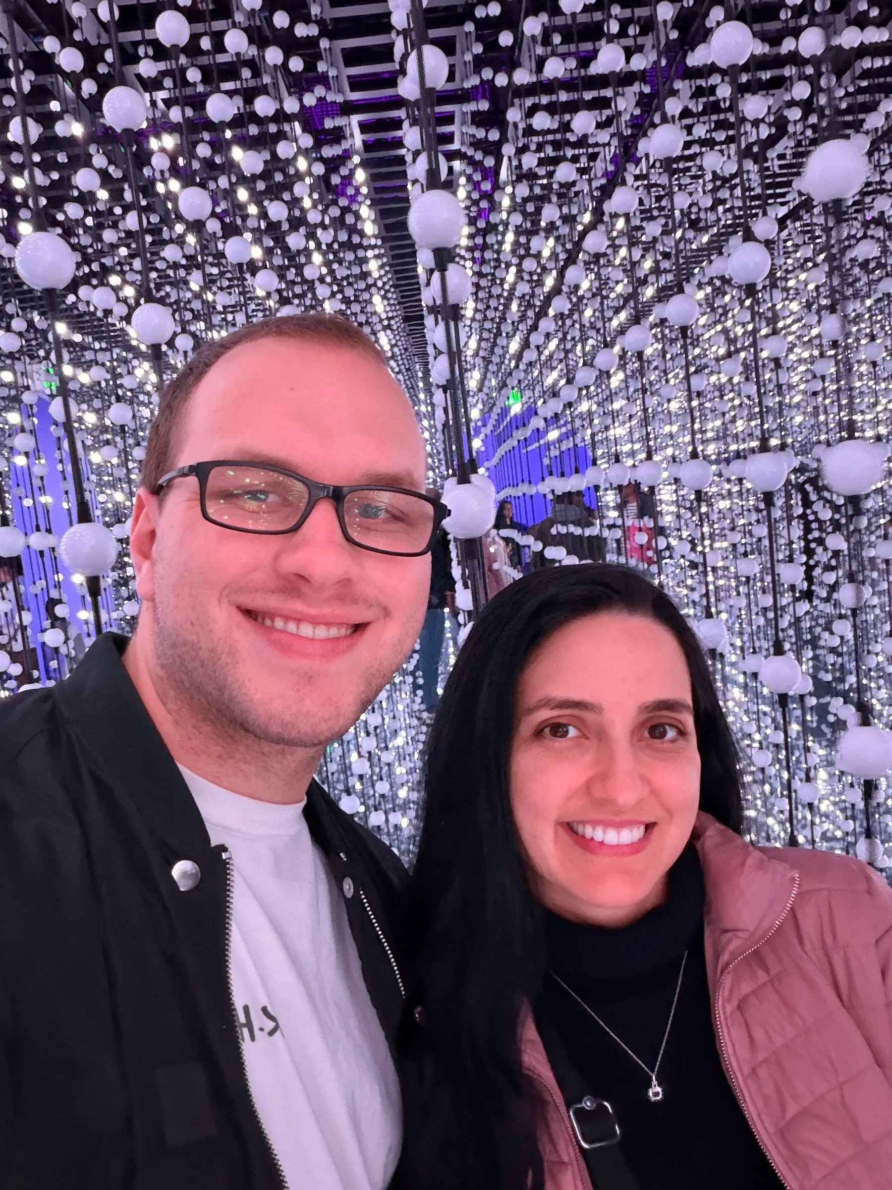 Tyler Henn and a companion taking a selfie inside a mirrored installation with hanging white lights
