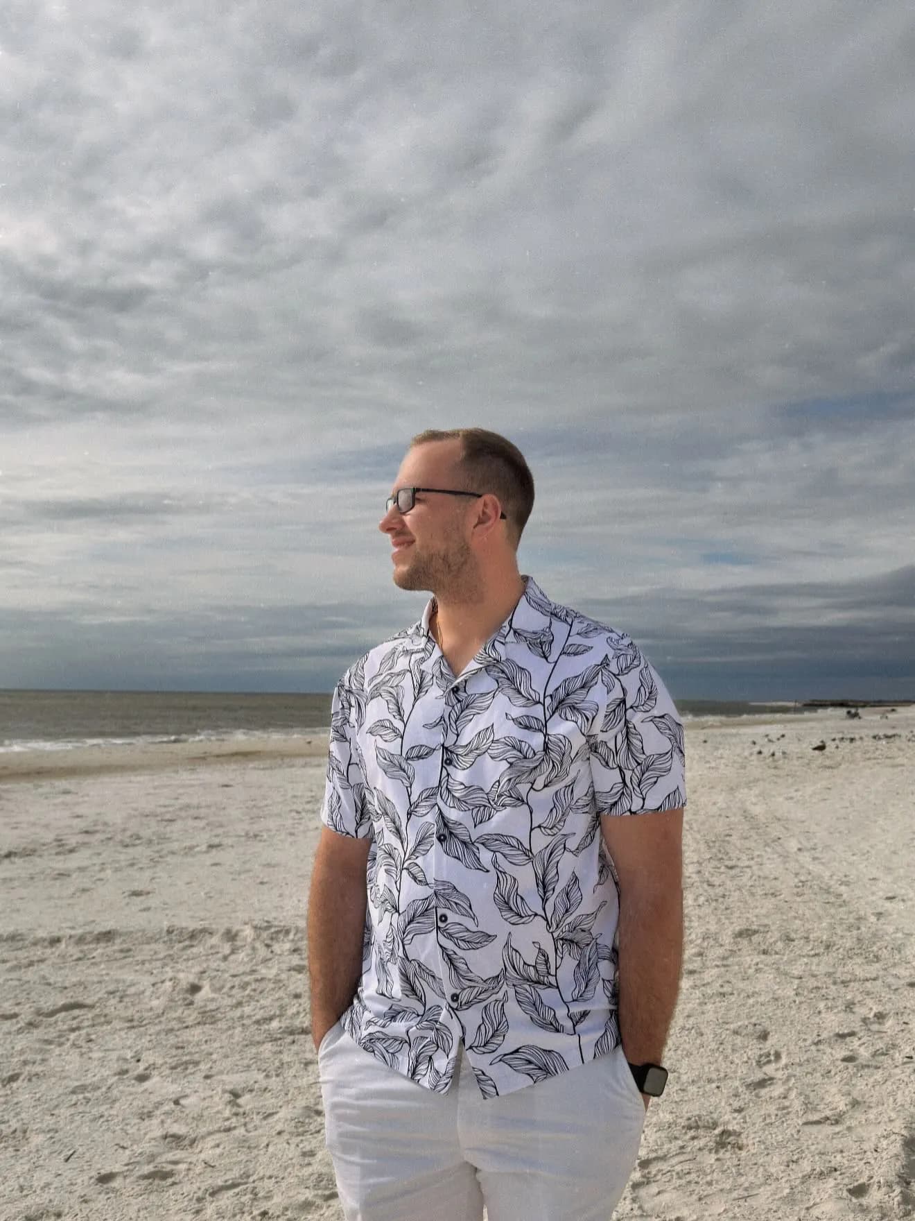 Tyler Henn standing on the sandy shore in Mexico Beach, Florida, beneath an overcast sky