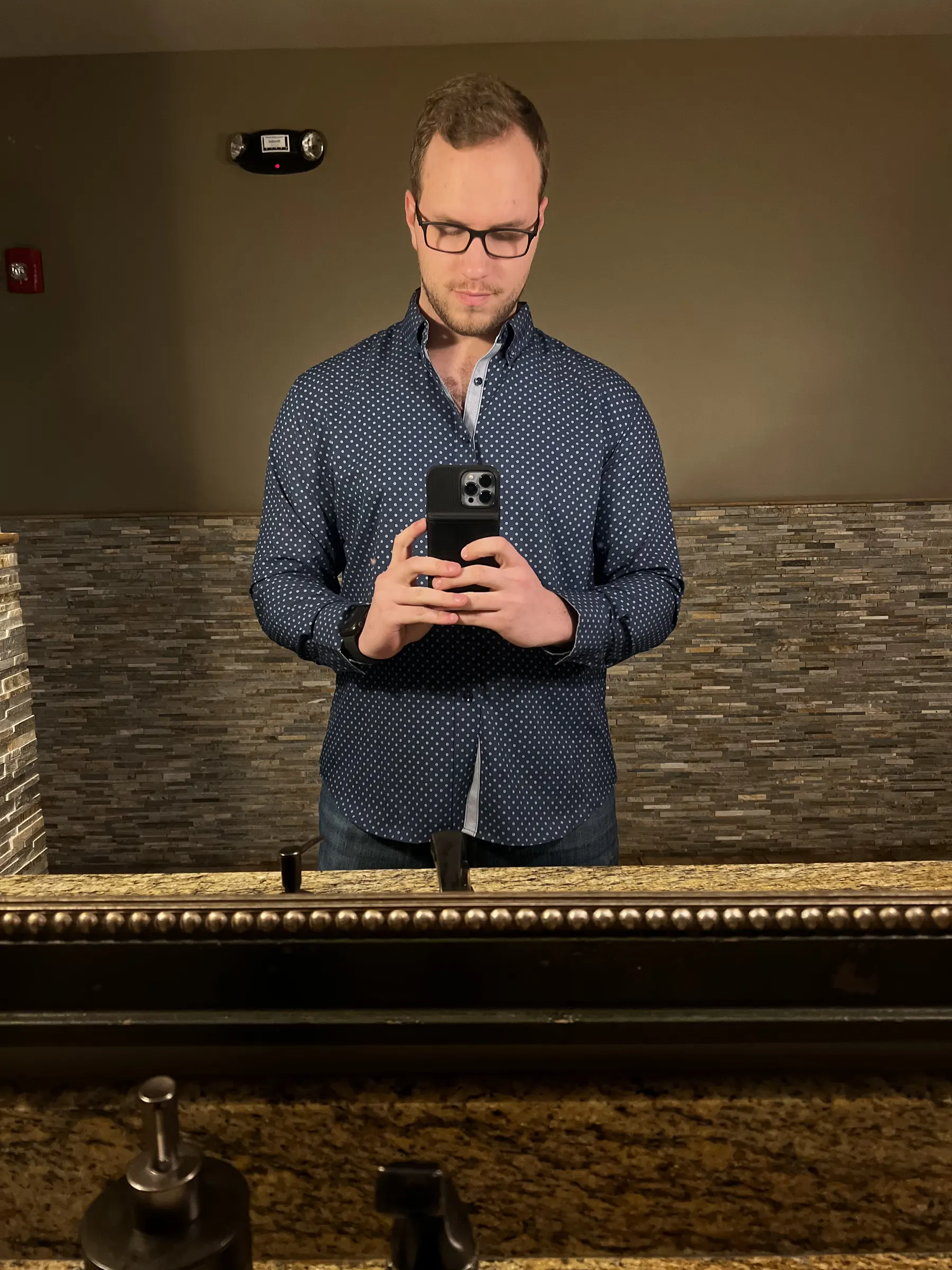 Tyler Henn taking a mirror selfie while wearing a navy blue patterned button-down shirt