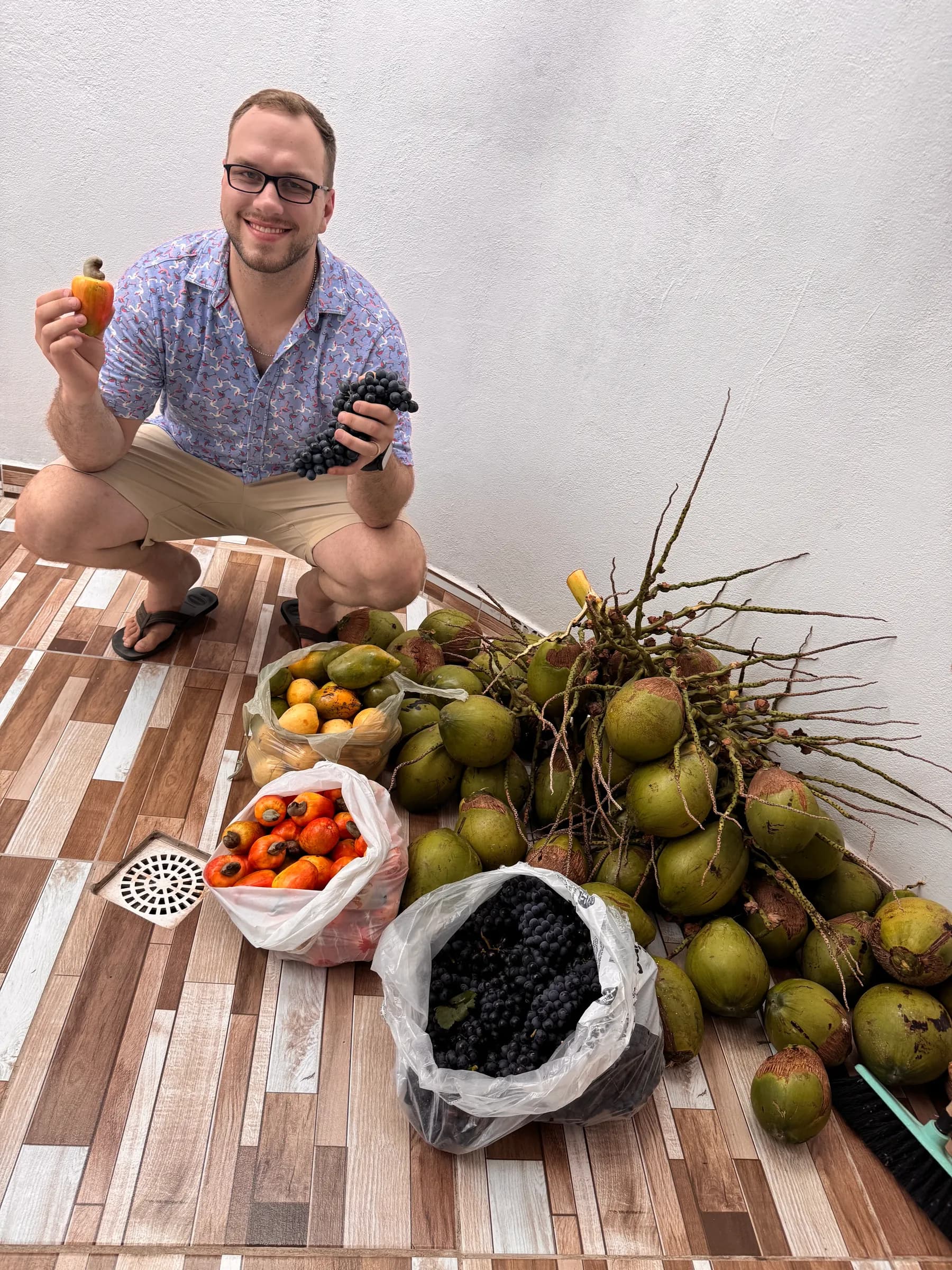 Tyler Henn crouching beside grapes, cashew fruit, coconuts, and other fresh fruit in Brazil