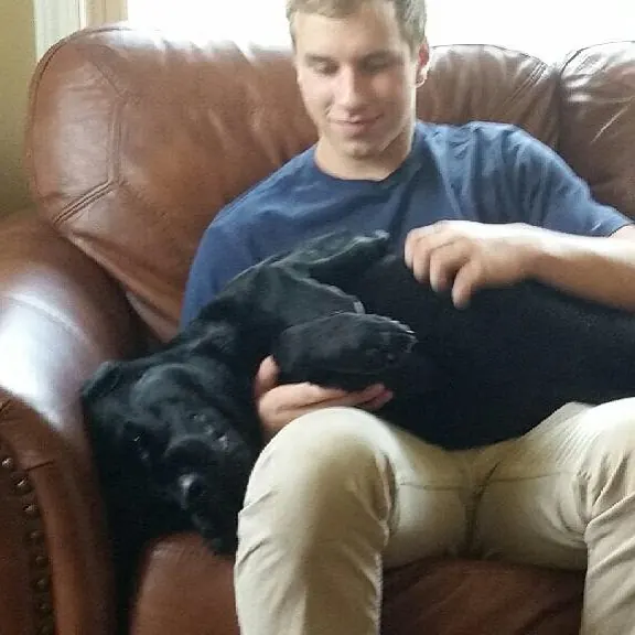 Tyler Henn sitting in a leather chair with his black dog, Koal, resting across his lap