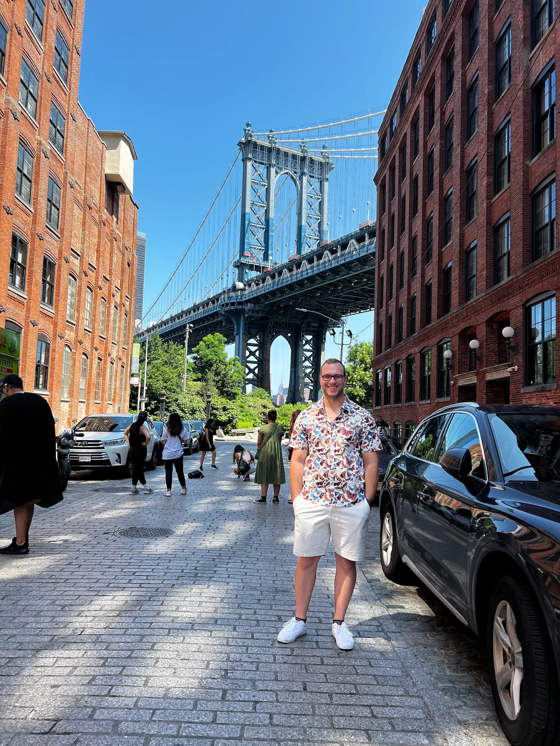 Tyler Henn standing in DUMBO, Brooklyn, with the Manhattan Bridge behind him